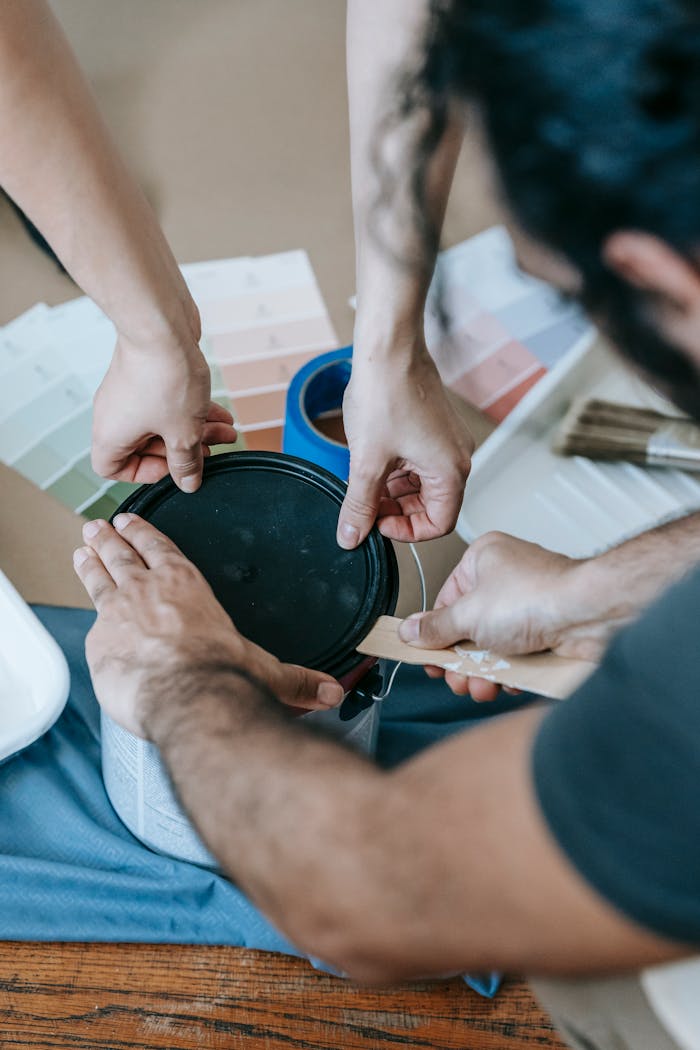 Two people collaborating on a home renovation project, opening a paint can with color swatches nearby.