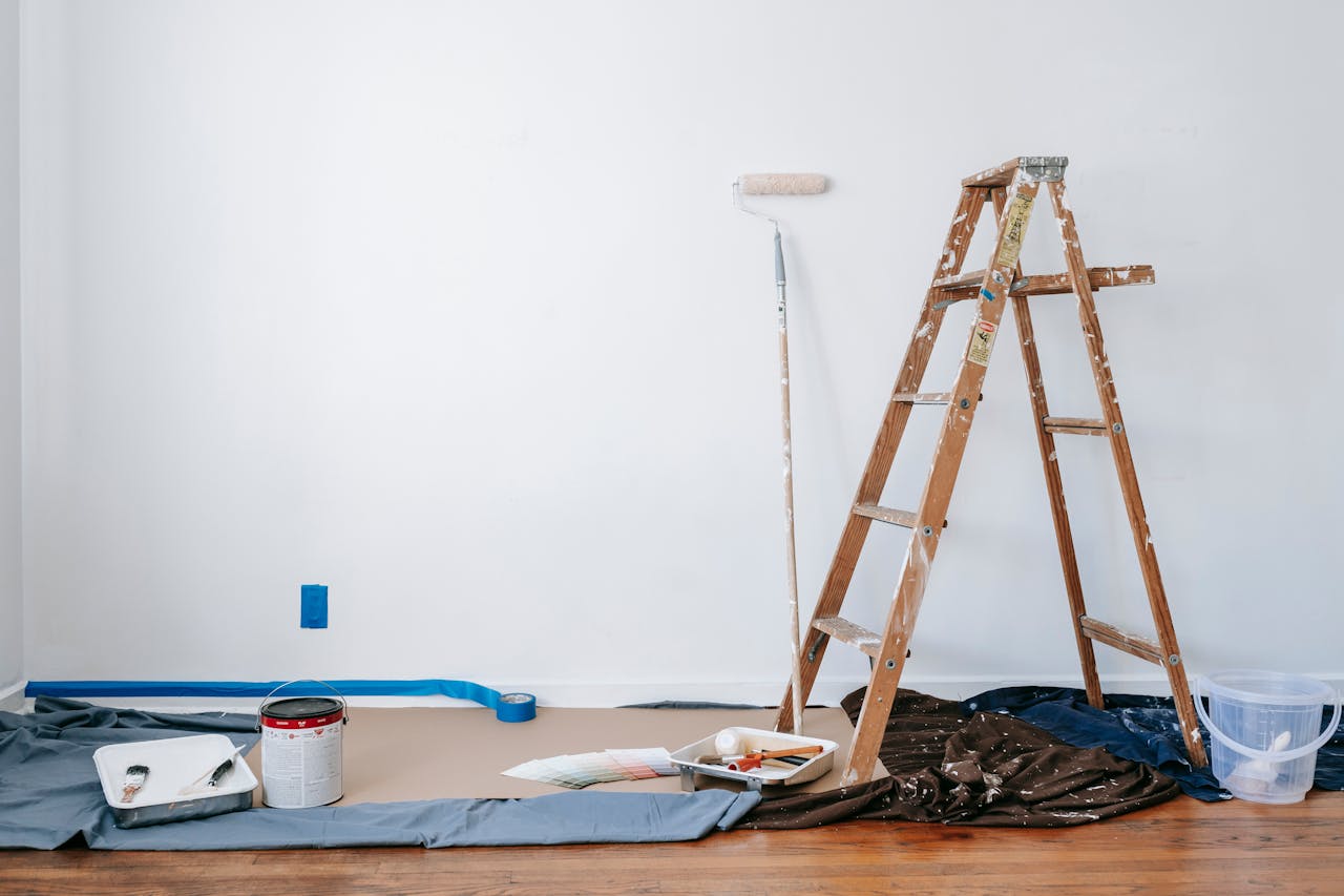 services-img A room prepared for renovation with a ladder, paint supplies, and drop cloth.